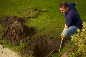 Man digging a hole in the yard with a shovel to access a water pipe.