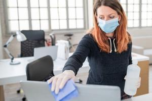 Woman wearing face mask disinfecting office equipment